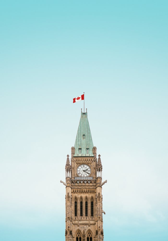 brown-and-white-concrete-building-under-blue-sky-3656756 The iconic Peace Tower in Ottawa, Canada, with a clear blue sky and Canadian flag.