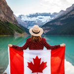Woman holding a Canadian flag at stunning Lake Louise, Alberta, embracing nature and patriotism.