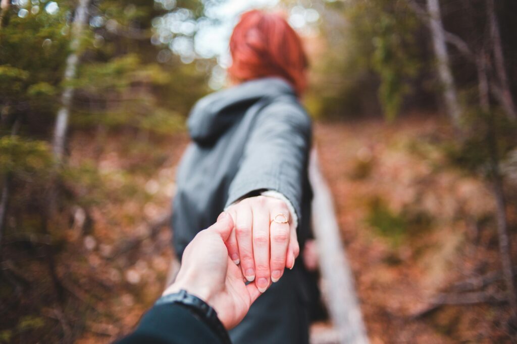A couple holding hands walking through a serene autumn forest setting.