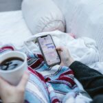 Person relaxing indoors with coffee and smartphone, texting in a cozy setting.